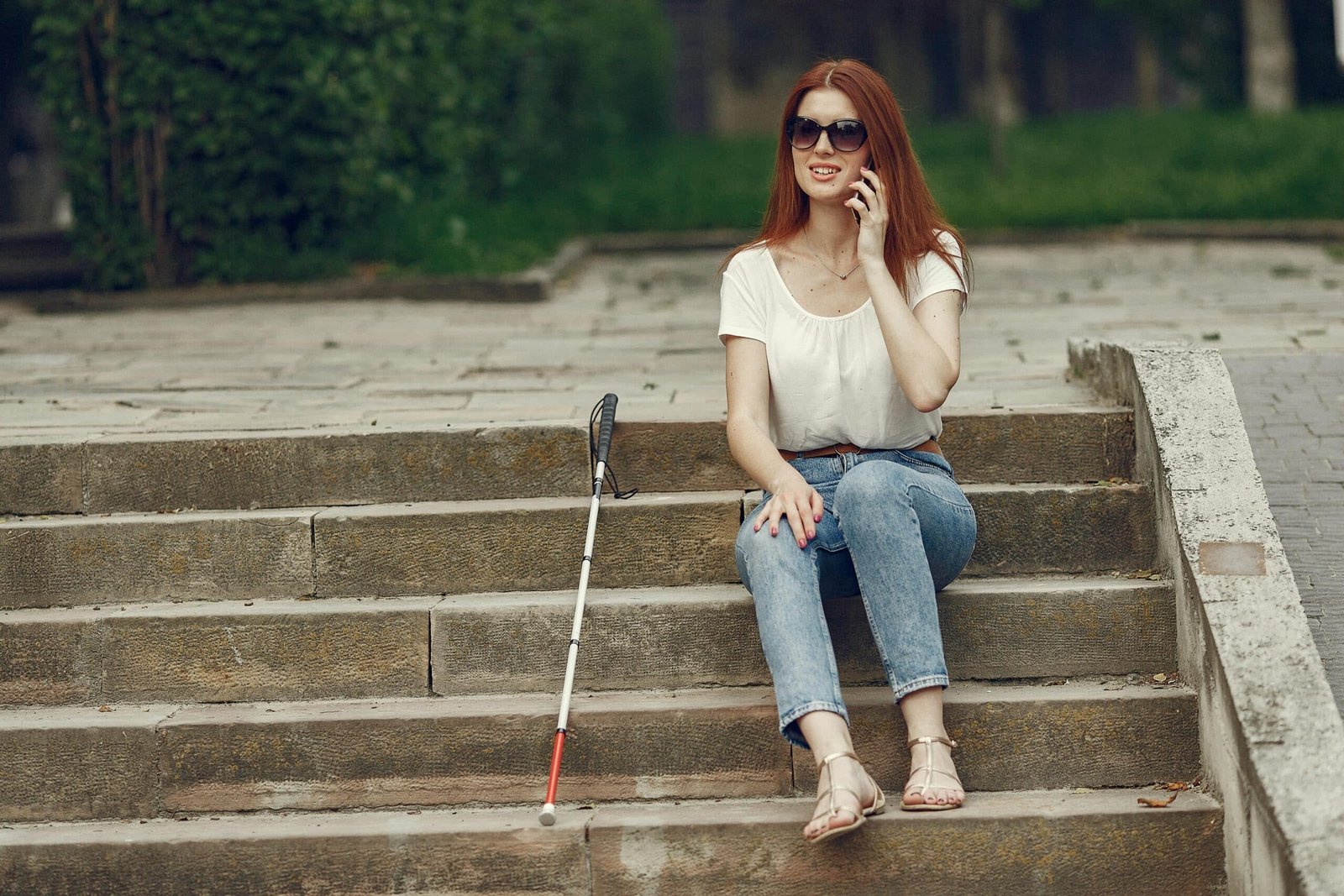 Visually impaired lady sitting outside with her white cane by her side. She could be navigating social media thanks to a screen reader.